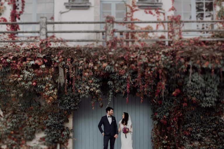 couple de mariés devant une porte de garage bleue et un mur de lieres sur un blacon