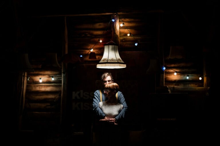 photo de couple posant dans une grange sous un lustre et des guirlandes colorées