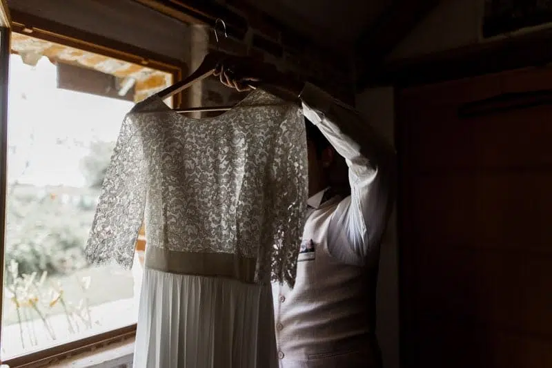 Homme portant sur un cintre, la robe de mariée devant une fenêtre