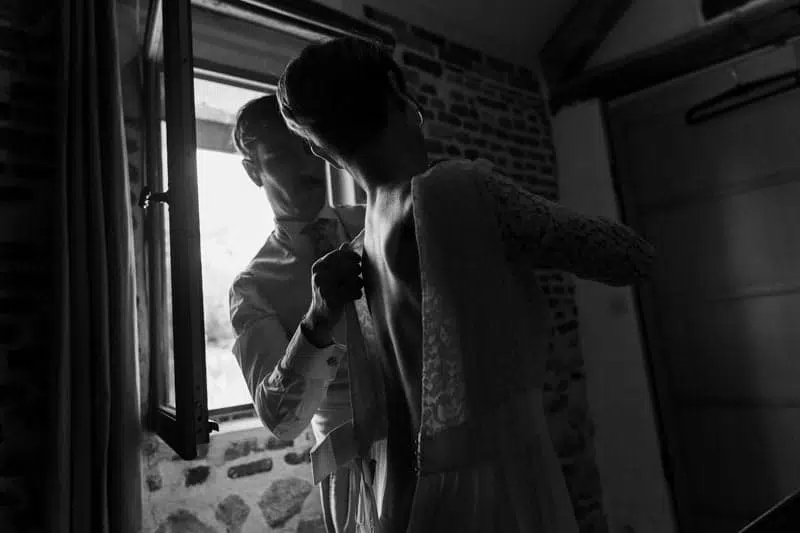 Photo, clair-obscur du Temoin revêtant la robe de la mariée devant une fenêtre