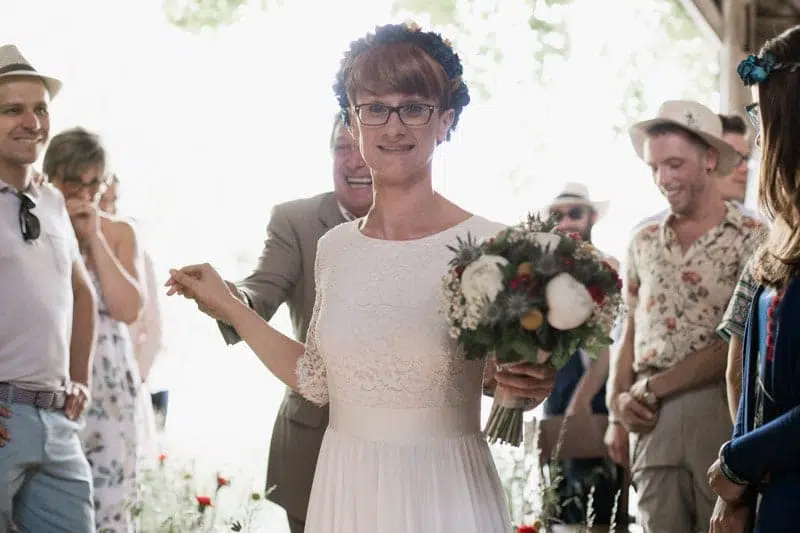 Entrée de la Mariée portant une couronne de fleurs, une robe blanche et un bouquet dans les mains