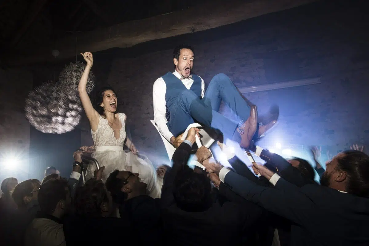 mariés assis sur une chaise et se faisant porter par les invités durant la soirée dansante