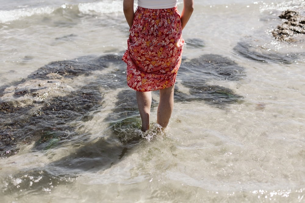 femme en jupe les pieds dans l'eau