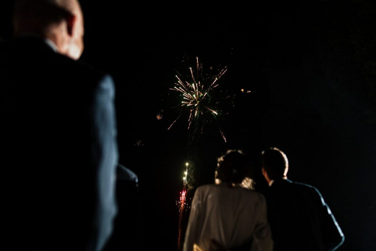 Feu d’artifice du mariage vu des invités – nuit noire, étincelles colorées.