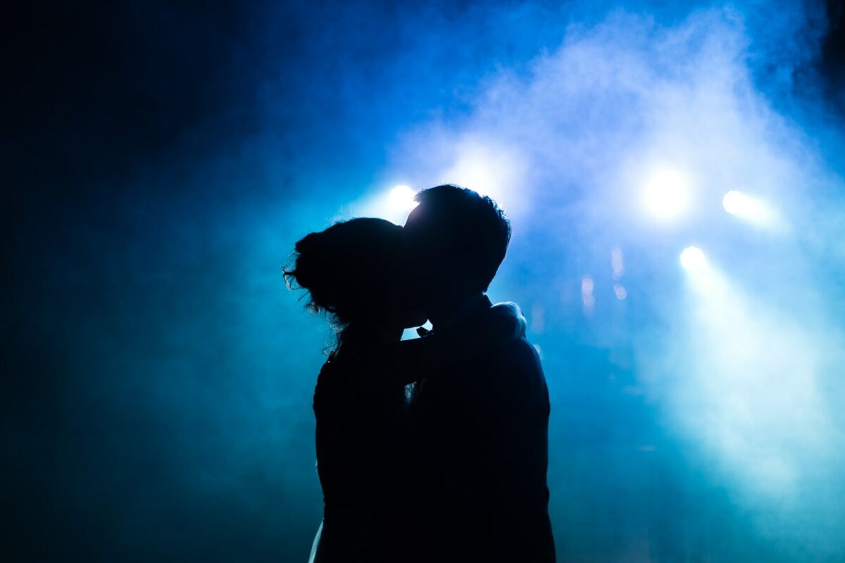 Silhouette des mariés qui s’embrassent sur la piste, fumée bleue et projecteurs en contre-jour.