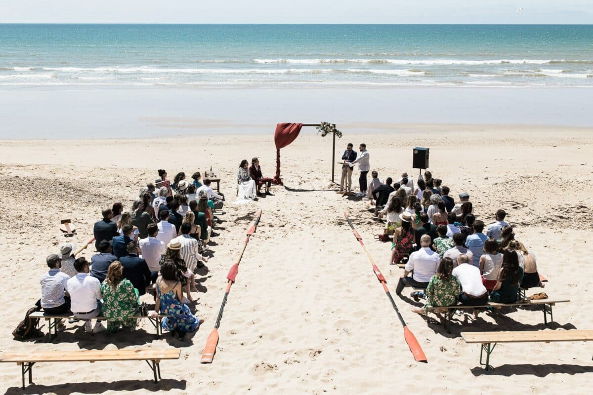 Vue d’ensemble de la cérémonie laïque sur la plage, arche rouge face à l’océan — Saint-Jean-de-Monts, Vendée.