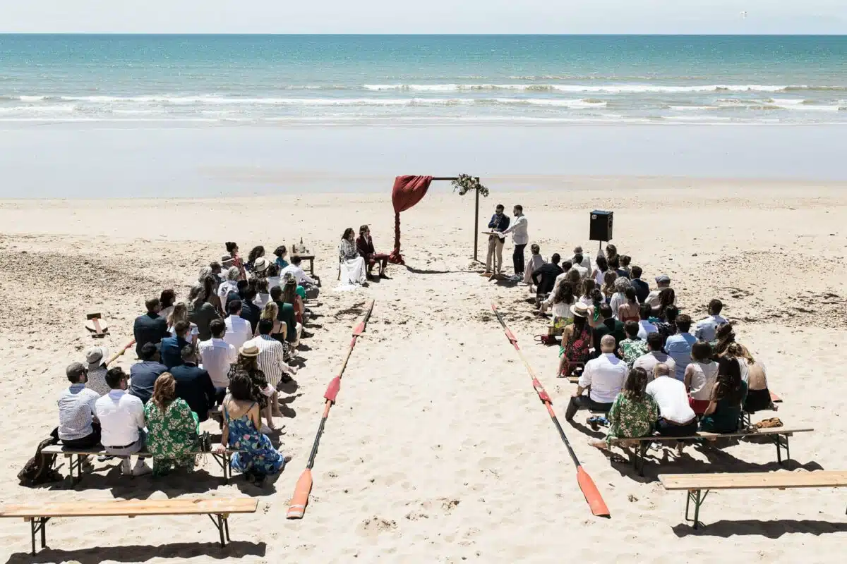 Vue d’ensemble de la cérémonie laïque sur la plage, arche rouge face à l’océan — Saint-Jean-de-Monts, Vendée.
