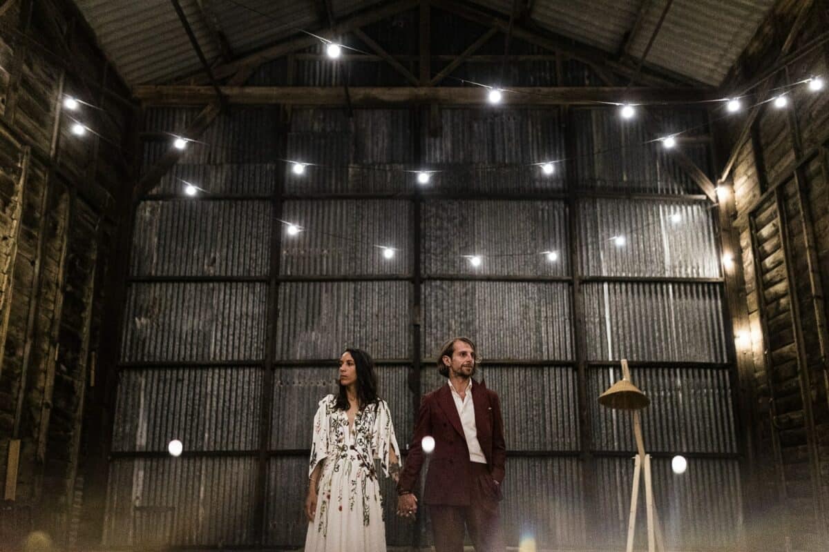 Portrait des mariés main dans la main sous guirlandes lumineuses dans une grange — domaine de la Bernerie, Froidfond.