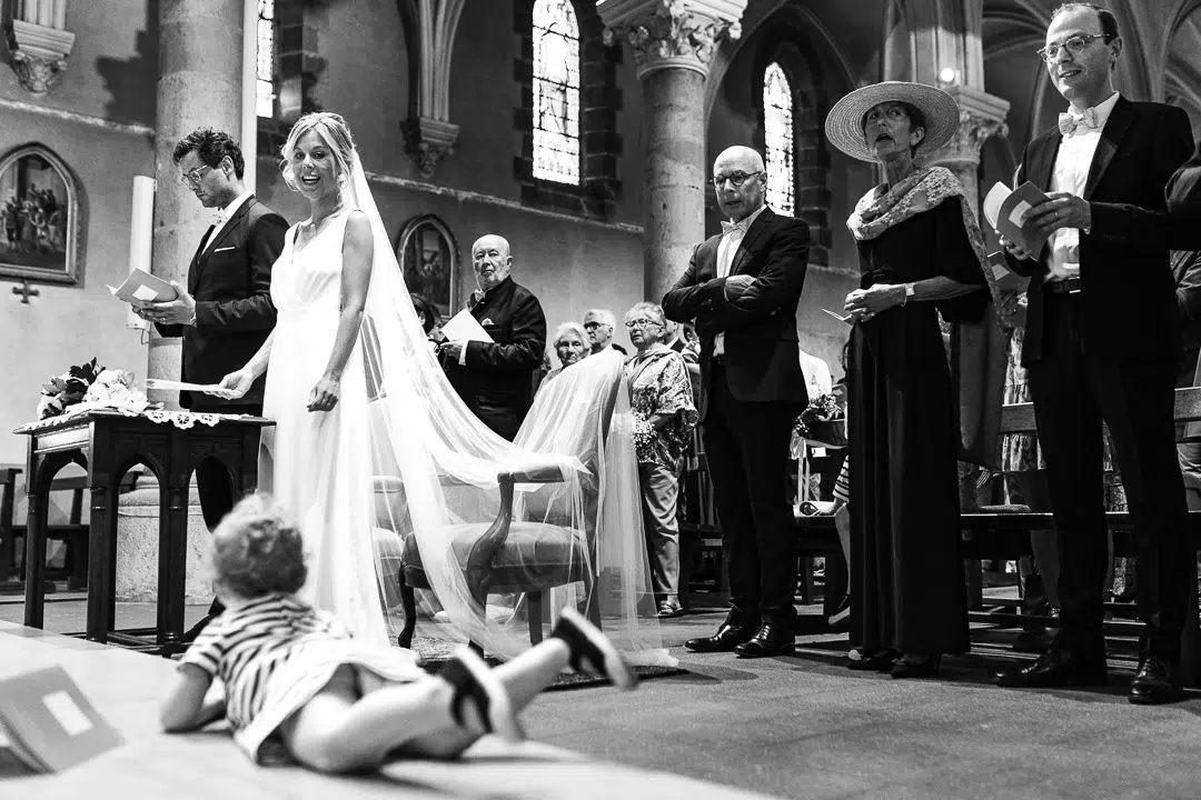 Reportage de mariage à l'eglise. Un enfant est allongé sur la marche de l'eglise. Les invités sourient.