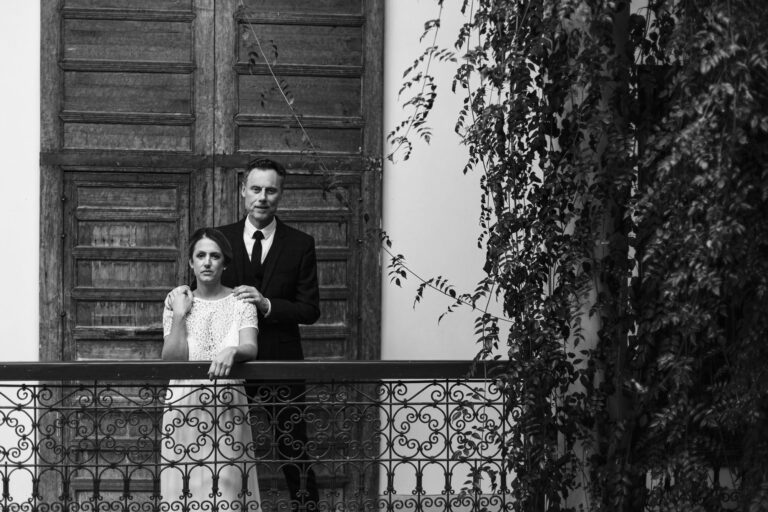 Portrait des mariés sur le balcon d’un riad, ferronnerie et portes en bois – mariage intimiste dans la médina au Maroc.