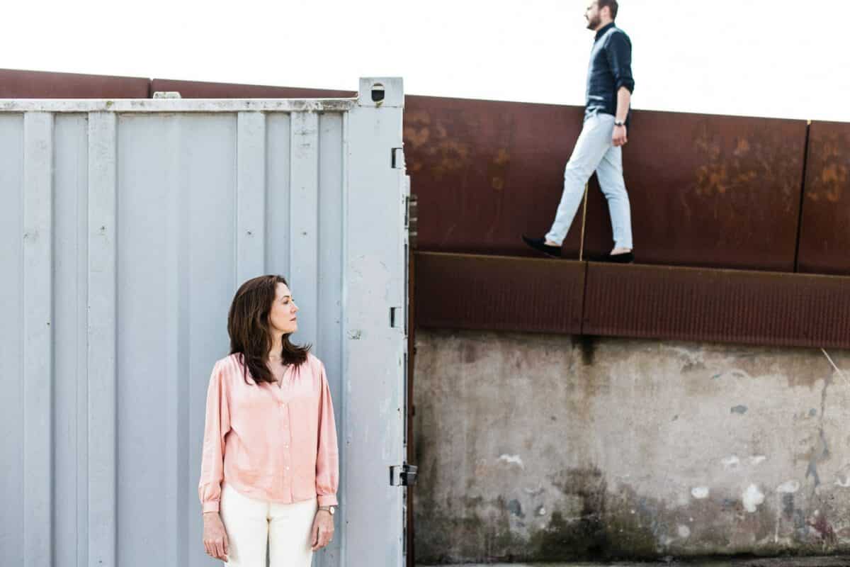 Composition graphique : elle près d’un container, lui marche sur le mur acier.