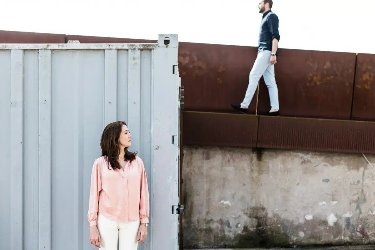 Composition graphique : elle près d’un container, lui marche sur le mur acier.
