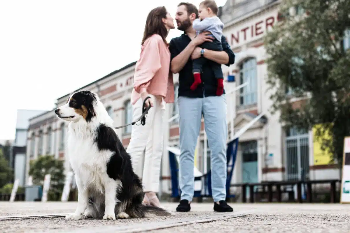 Chien assis au premier plan, couple s’embrassant avec leur enfant devant les nefs.