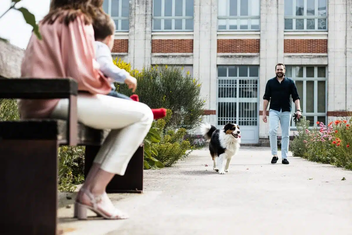Le chien court vers la mère assise, père en arrière-plan devant les nefs.