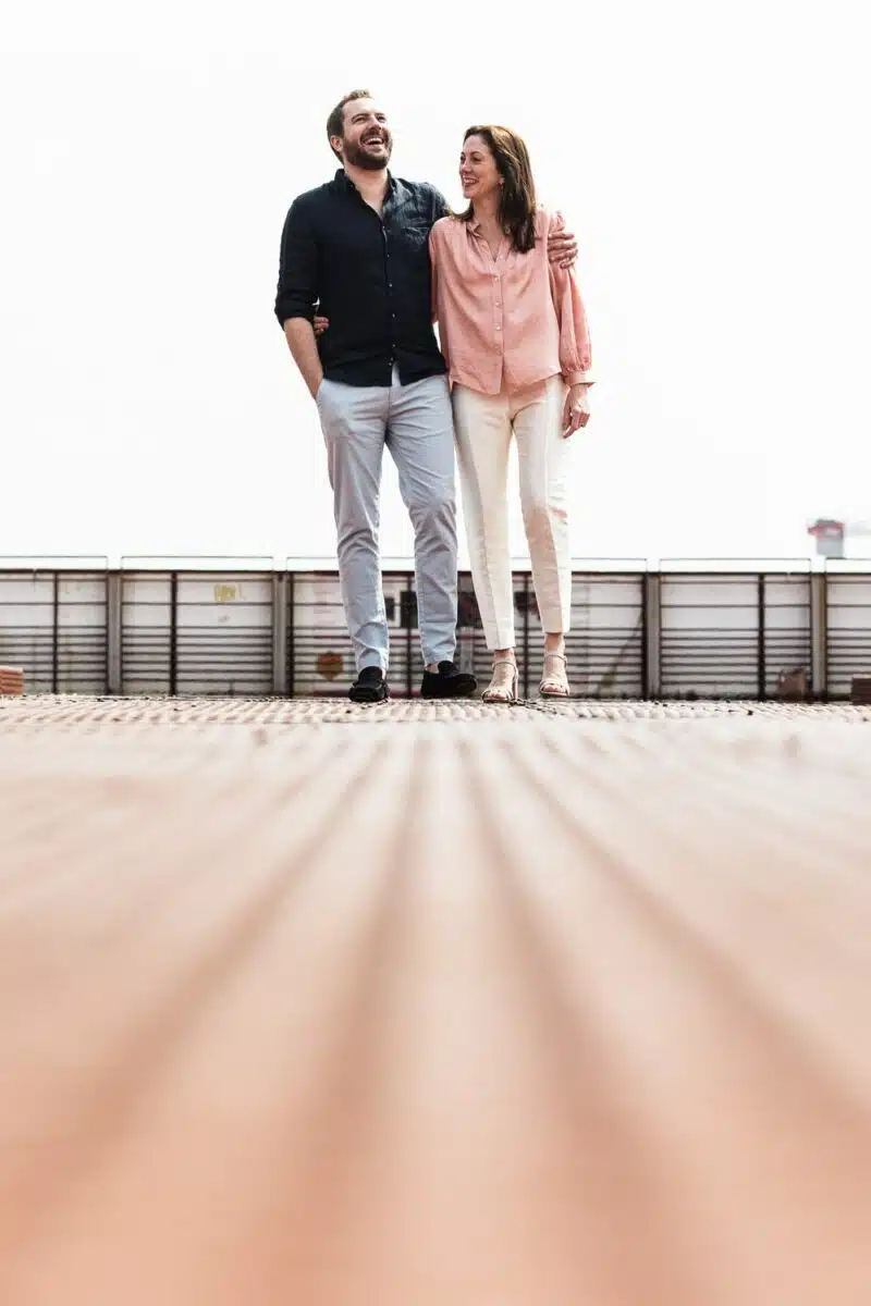 Couple riant bras dessus bras dessous, sur passerelle métallique rouillée.