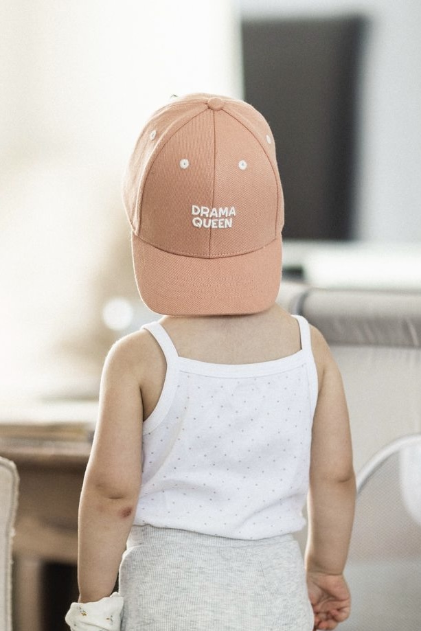 petit fille de dos dans un salon avec la casquette a l'envers et inscrit dessus Drama Queen