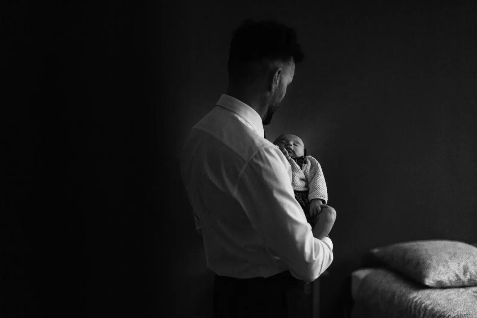Reportage mariage : un invité tenant un nouveau-né dans ses bras, photo en clair-obscur noir et blanc.