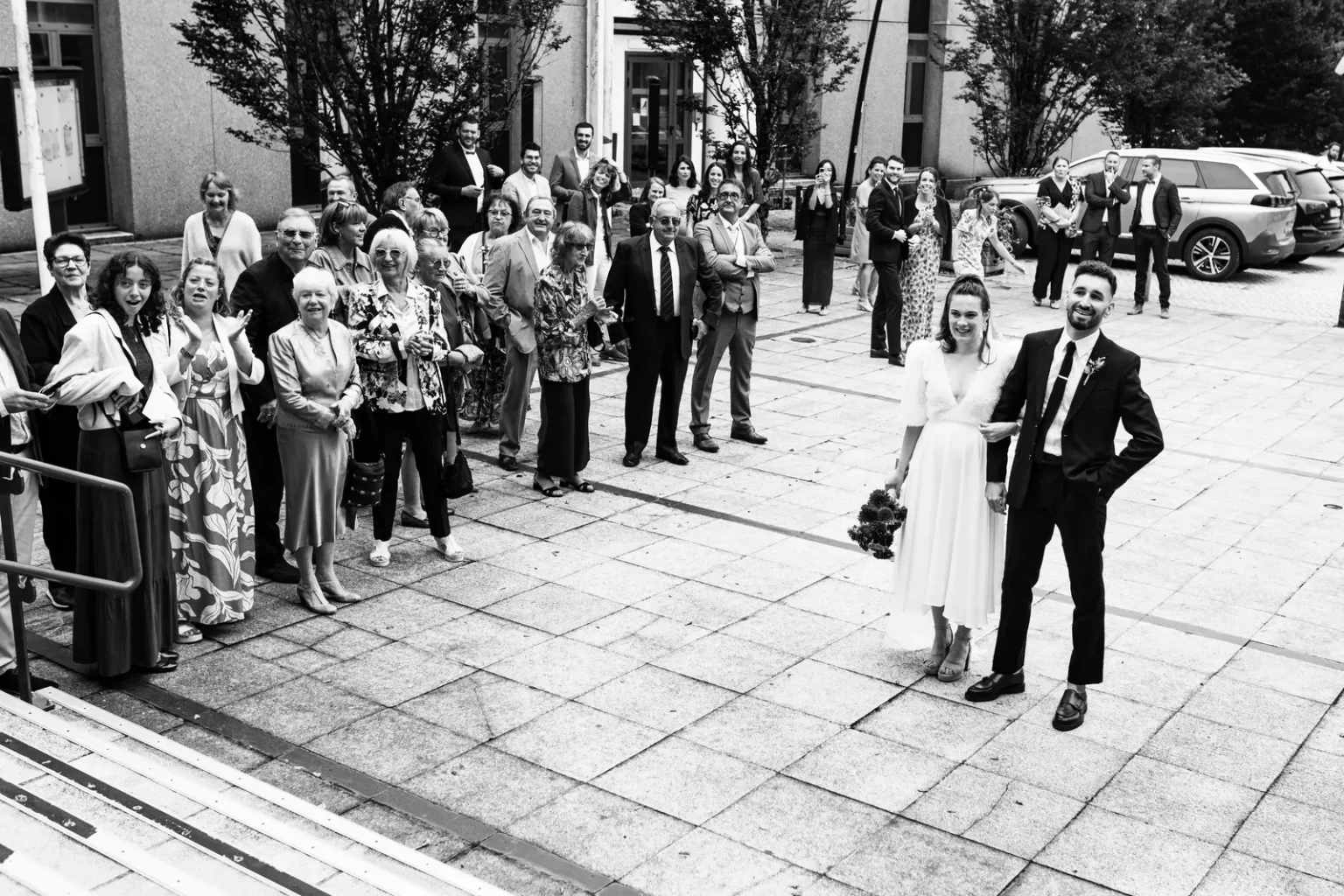 Sortie de cérémonie de mariage au Château de la Forêt, les mariés entourés de leurs invités en noir et blanc.