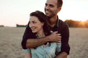 Portrait naturel et spontané d'un couple s'enlaçant sur les bords de Loire au coucher du soleil, avec une lumière dorée mettant en valeur leurs sourires.