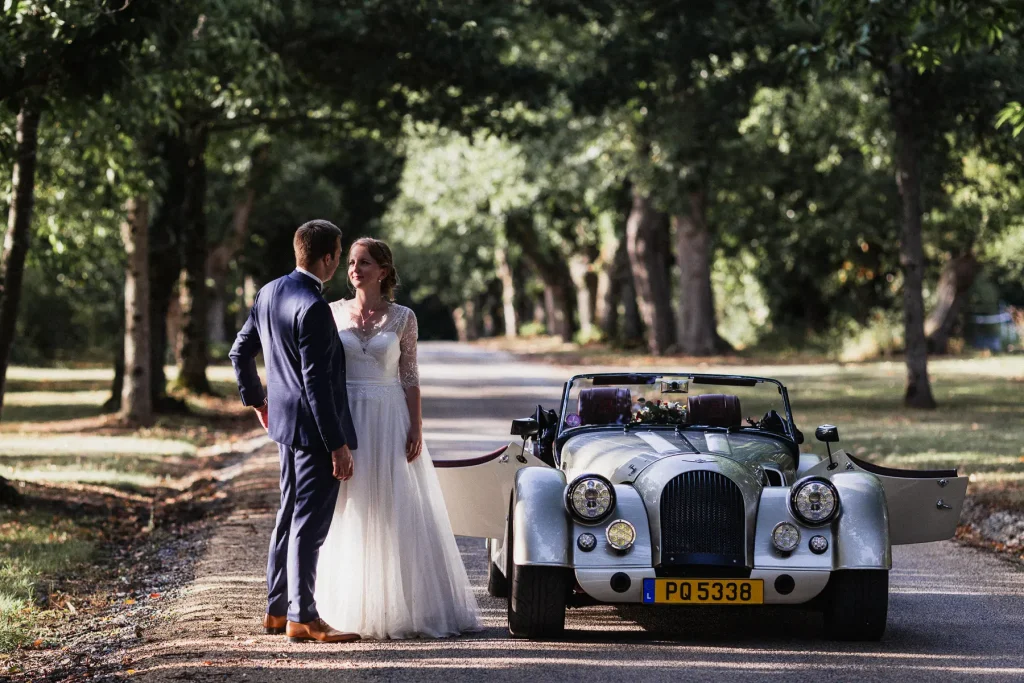 photo d'un couple de mariés a coté d'une voiture ancienne dans l'allée du domaine d'abbaretz