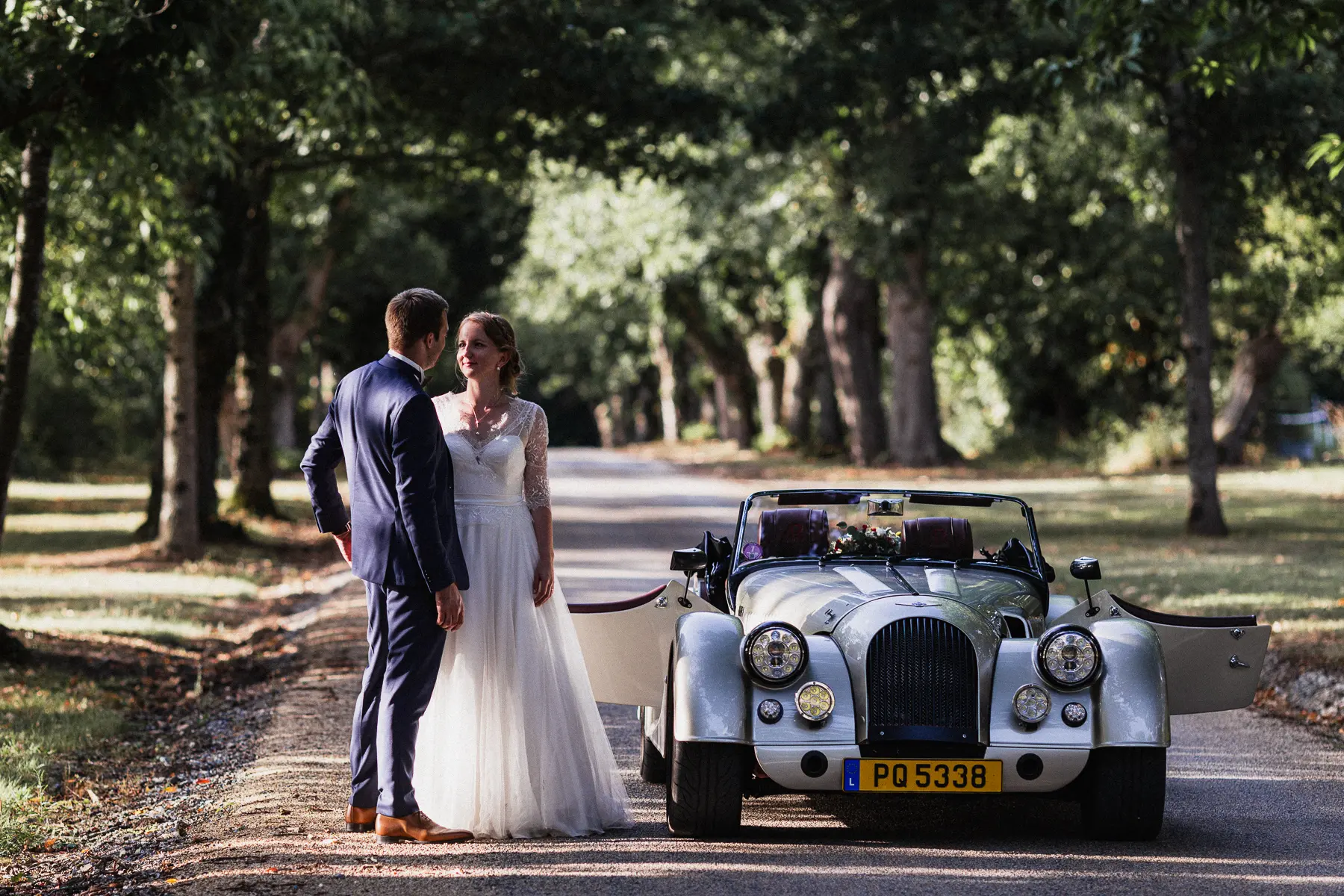 photo d'un couple de mariés a coté d'une voiture ancienne dans l'allée du domaine d'abbaretz