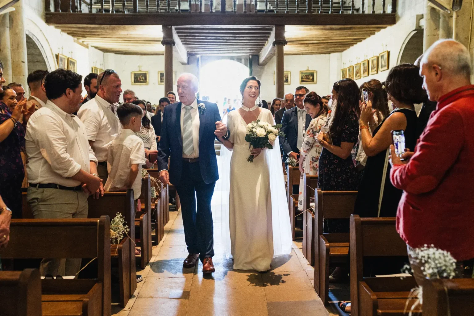 Entrée de la mariée au bras de son père dans l'église du Domaine de Roiffé, moment solennel capturé sur le vif.