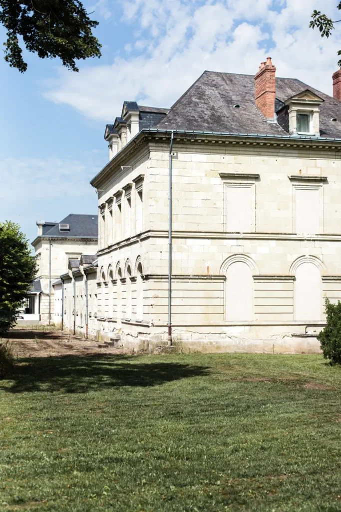 Façade latérale en pierre de tuffeau du Domaine de Roiffé sous un ciel bleu, photographie d'architecture de mariage.