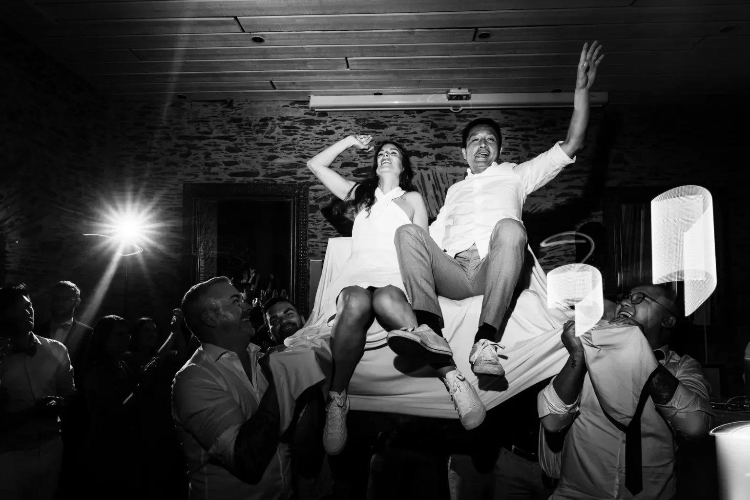 Ambiance de soirée de mariage en noir et blanc avec les mariés portés sur des chaises par les invités au château de la Jahotière.