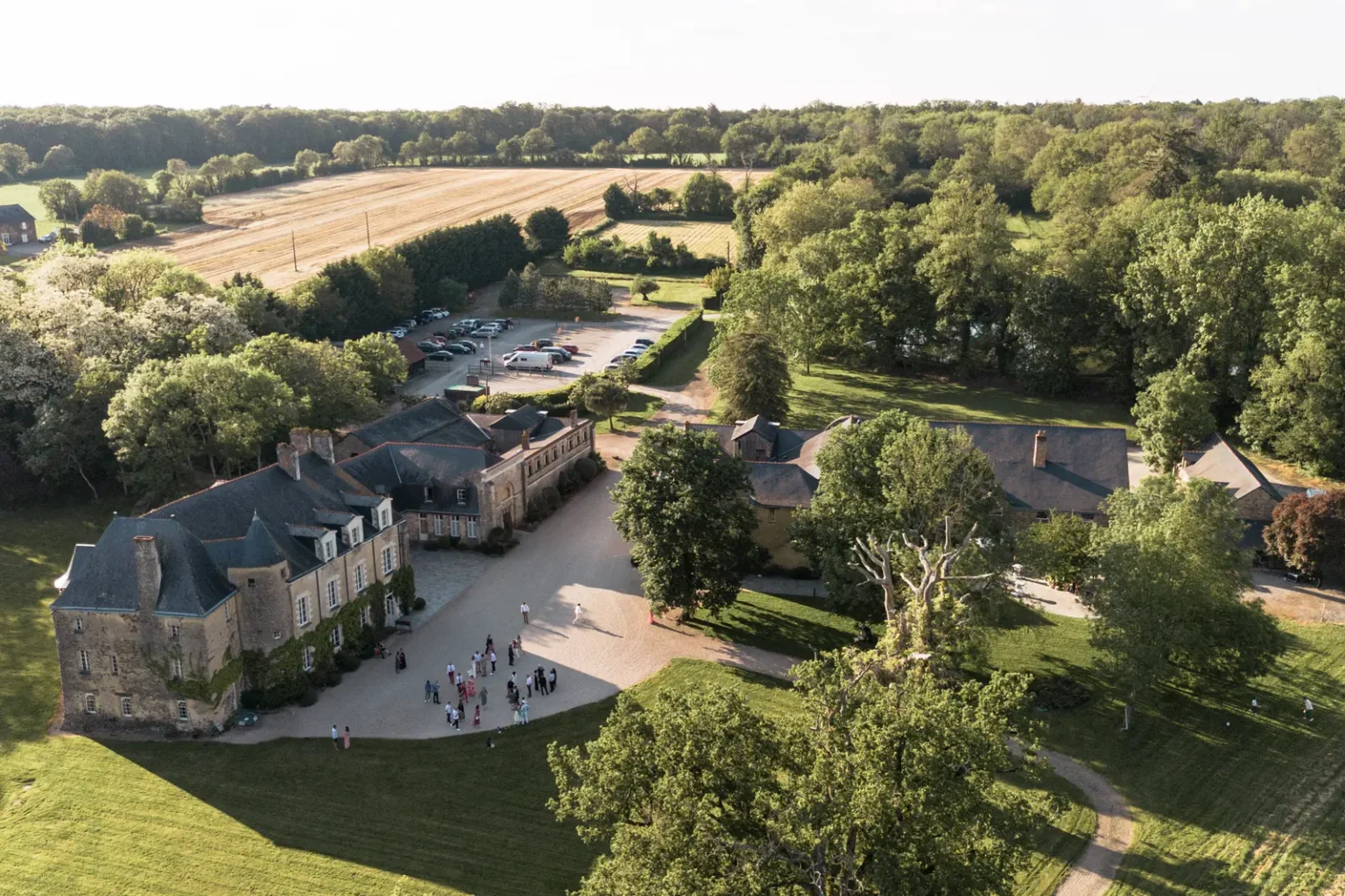 Vue aérienne par drone du Domaine de la Jahotière à Abbaretz, montrant les bâtiments historiques en pierre, les invités dans la cour et la campagne environnante.
