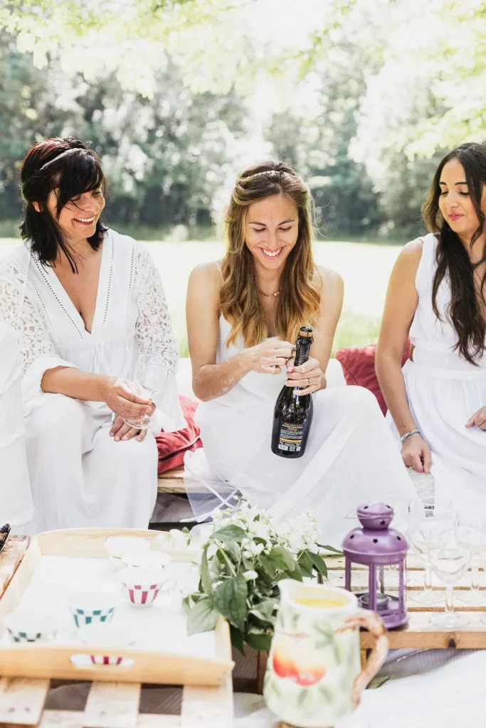 Future mariée ouvrant une bouteille de champagne pendant un brunch à l'ombre d'un arbre