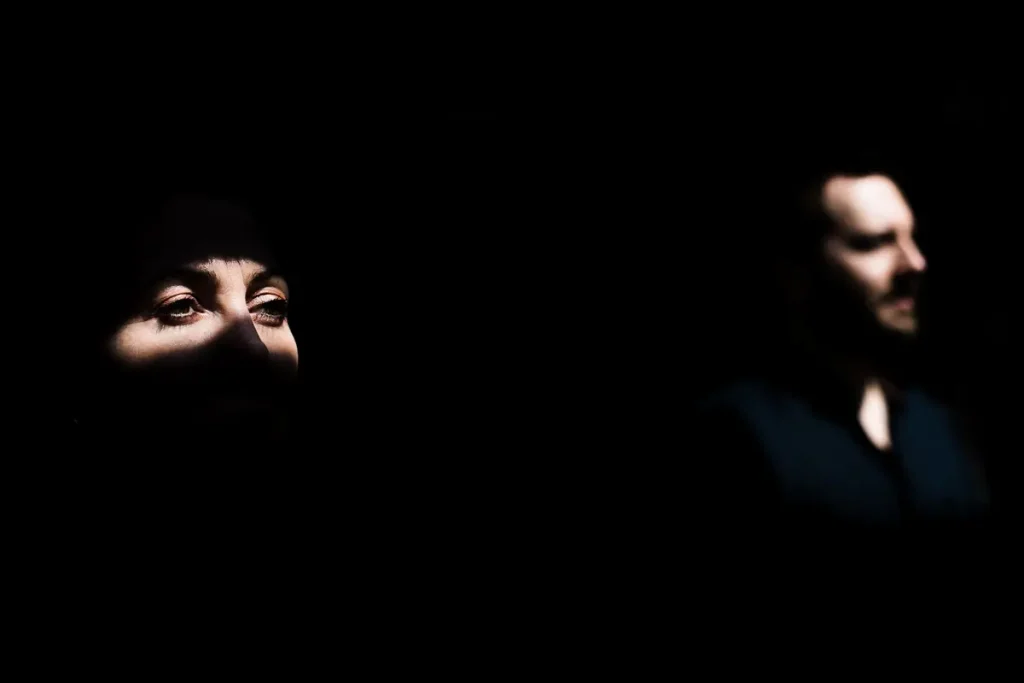 Portrait artistique en clair-obscur d'un couple dans l'ombre, mettant en lumière le regard d'une femme et le profil flou d'un homme aux maxhines de l'ile à Nantes.