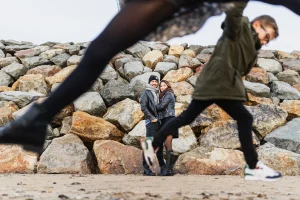 couple sur la plage devant une digue de pierre avec les enfants qui passent au premier plan