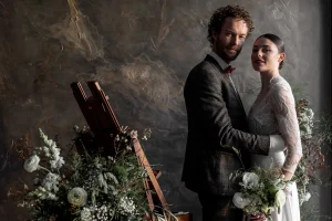 couple en séance photo au domaine de beaucé à Ligné. Ils posent devant un mur texturé avec des bouquets au premier plan