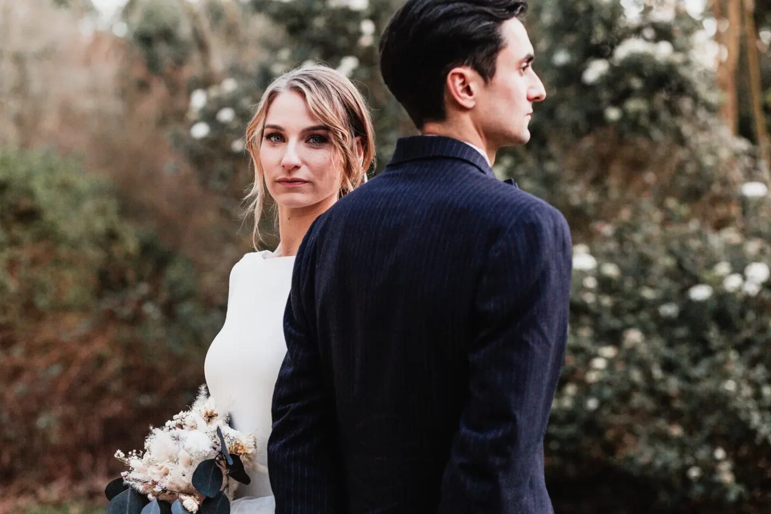 Portrait artistique des mariés en extérieur : la mariée regarde l'objectif tandis que le marié est de dos.