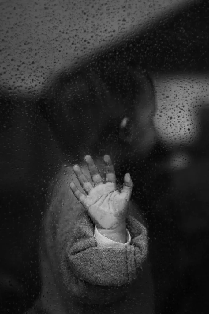 La main d'une petite fille posé sur une vitre avec des gouttes de pluie. Photo nostalgique en noir et blanc