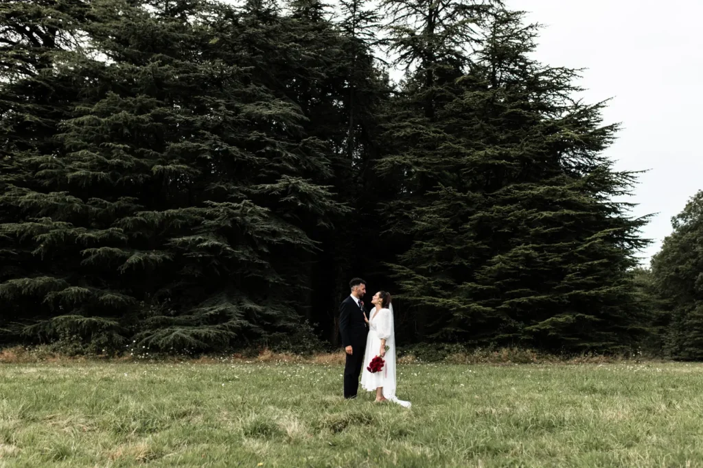 couple de mariés dans le parc du chateau de la foret au cellier devant des sapins