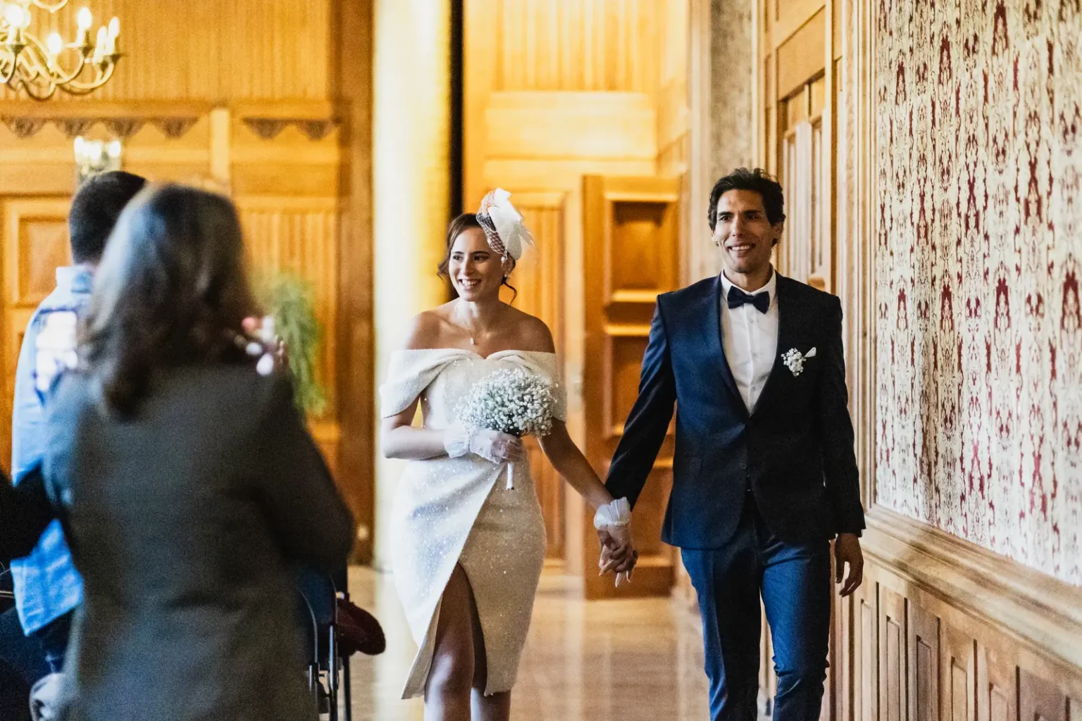 Mariés souriants marchant main dans la main dans la salle d'honneur boisée de la mairie de Nantes.