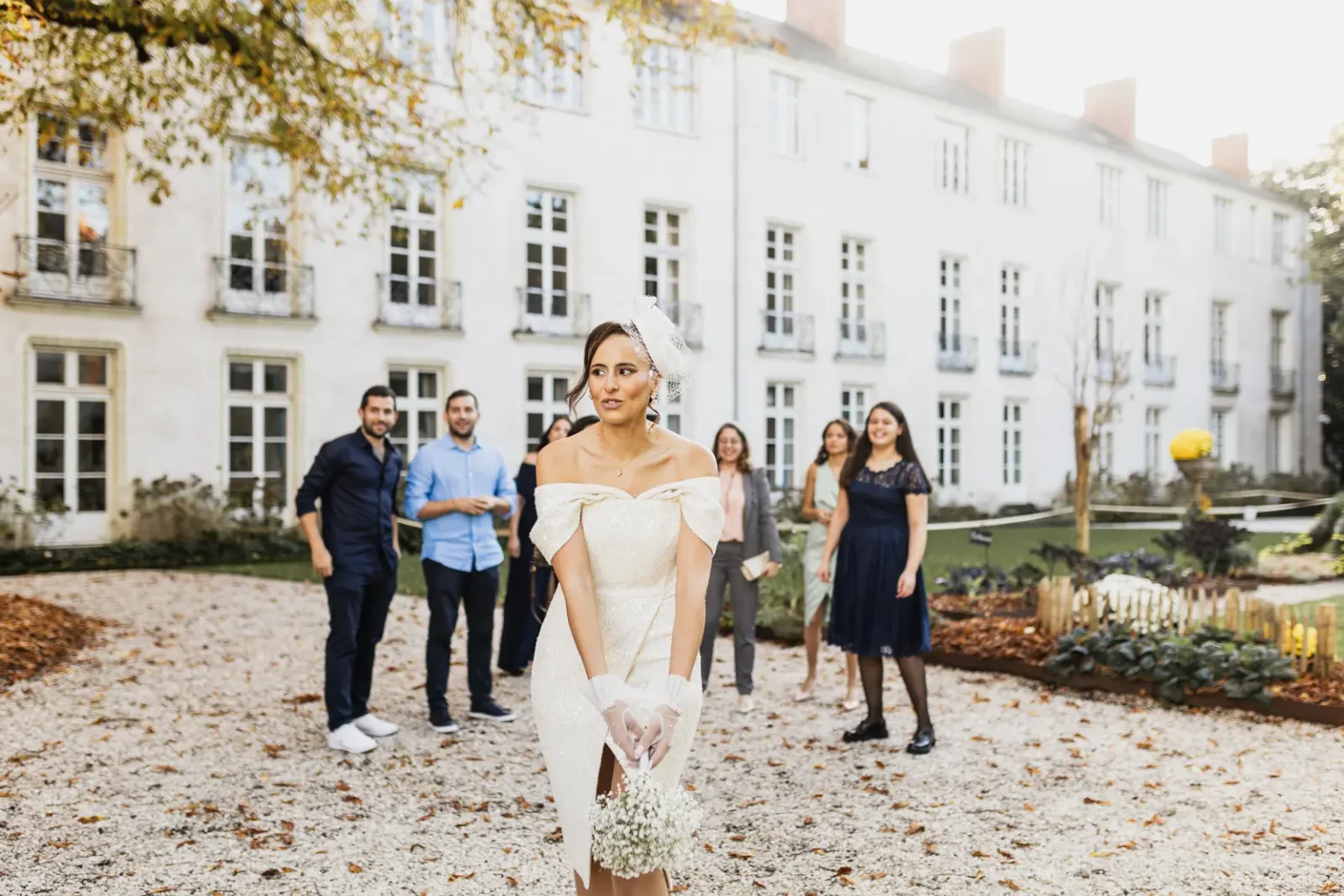 Mariée en robe blanche moderne s'apprêtant à lancer son bouquet de fleurs blanches à ses invités en extérieur.