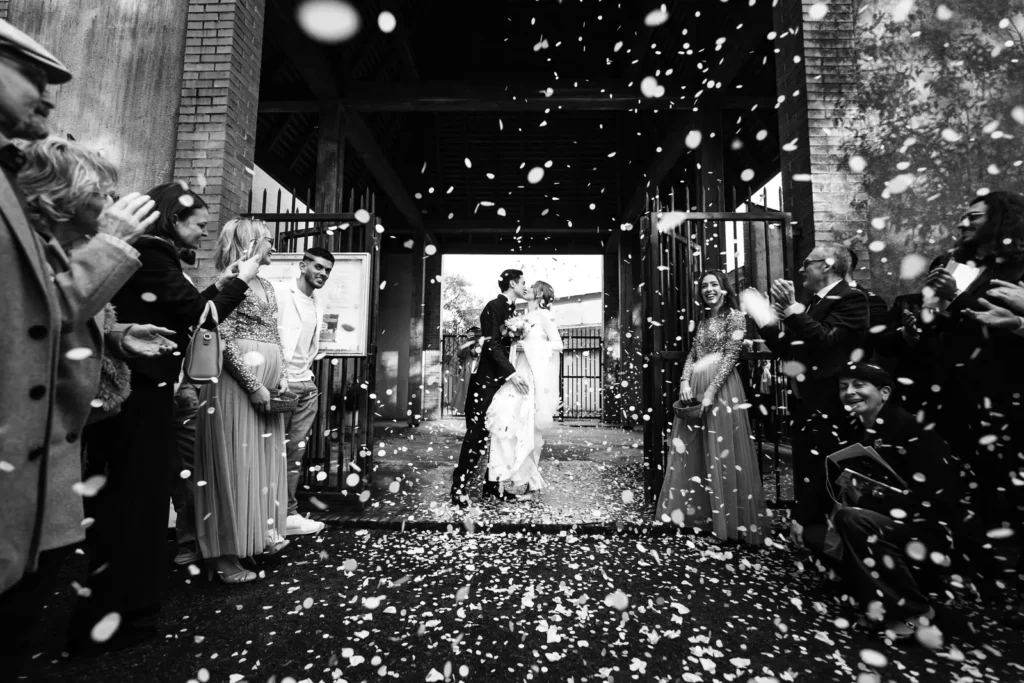 photographe de mariage à Nantes Sortie de cérémonie de mariage, les mariés s'embrassent derrière un portail en fer, photo noir et blanc.