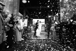 photographe de mariage à Nantes Sortie de cérémonie de mariage, les mariés s'embrassent derrière un portail en fer, photo noir et blanc.