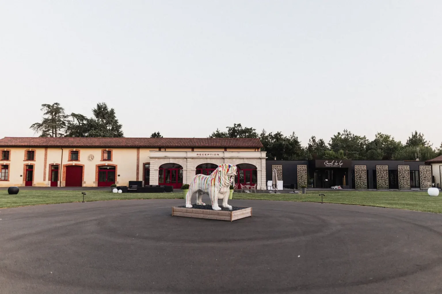 Vue extérieure du Domaine des Lys à Ancenis au crépuscule, avec sa sculpture de chien coloré au centre de la cour et la réception en façade