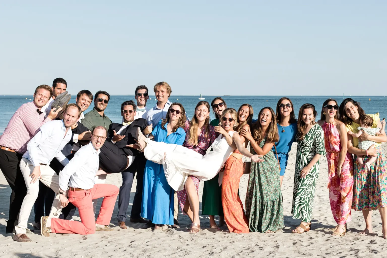 Photo de groupe festive sur la plage de La Baule avec les invités soulevant la mariée devant l'océan.